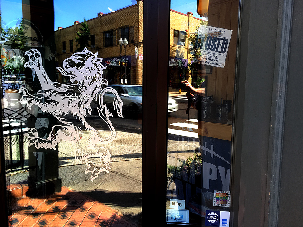 The 100% sign is seen in the entryway to Old State Clothing company, a Penn State souvenier store. A bold logo of a rampant lion is visible on the door.